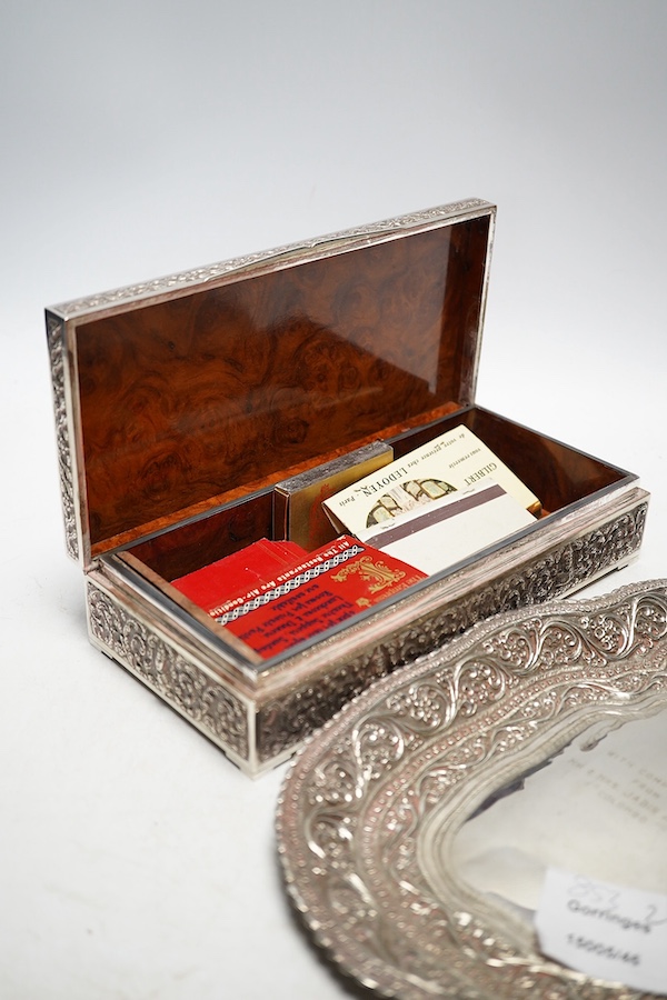 A Thai white metal cigarette box, wood lined, stamped Thainakon, 20cm and a Ceylonese white metal dish, shaped in the form of the country, with embossed borders, and inscription, maker’s mark SS, 24.7cm long, 182g. Condi